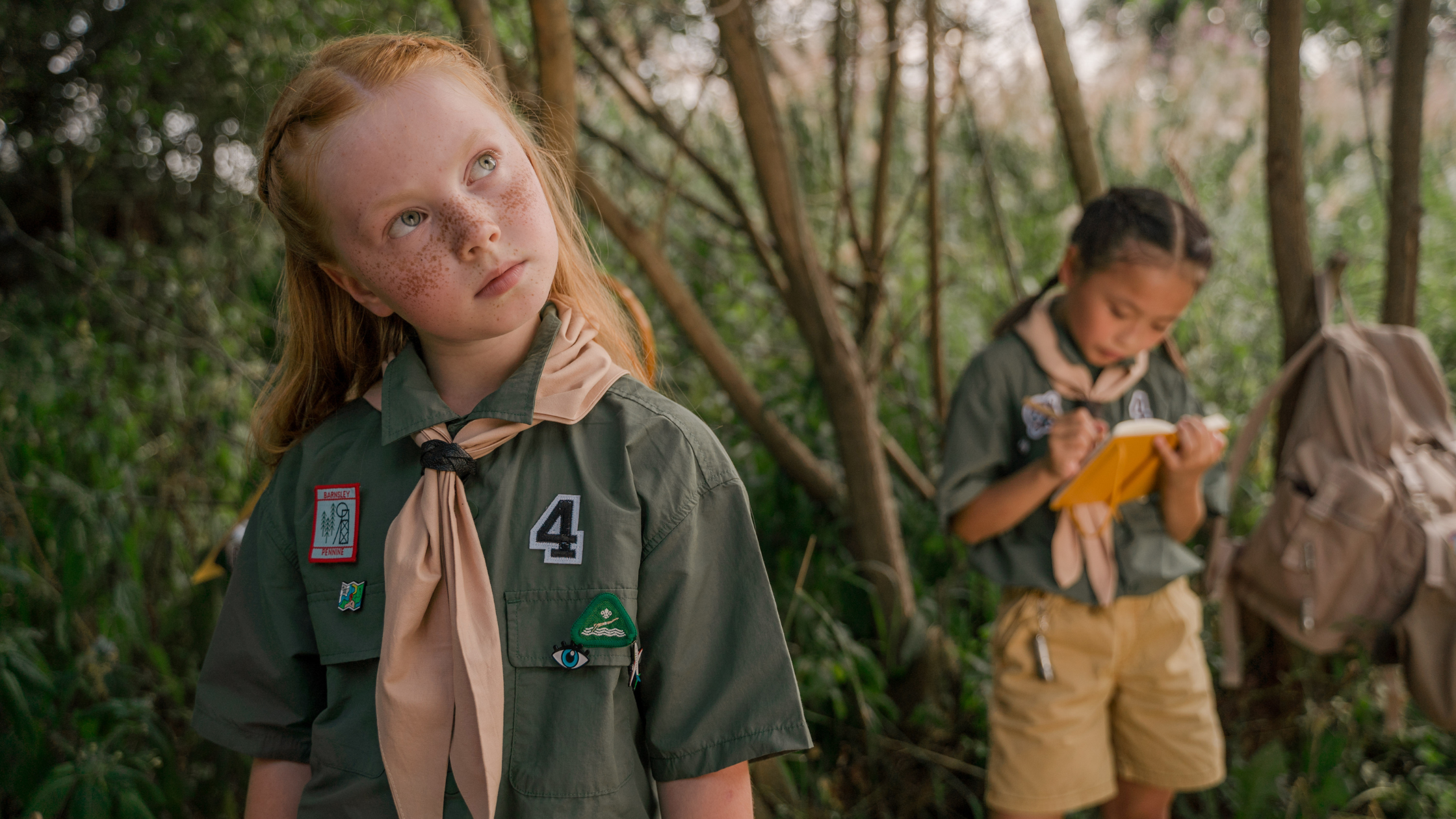 Two girl scouts in uniform thinking hard in the woods