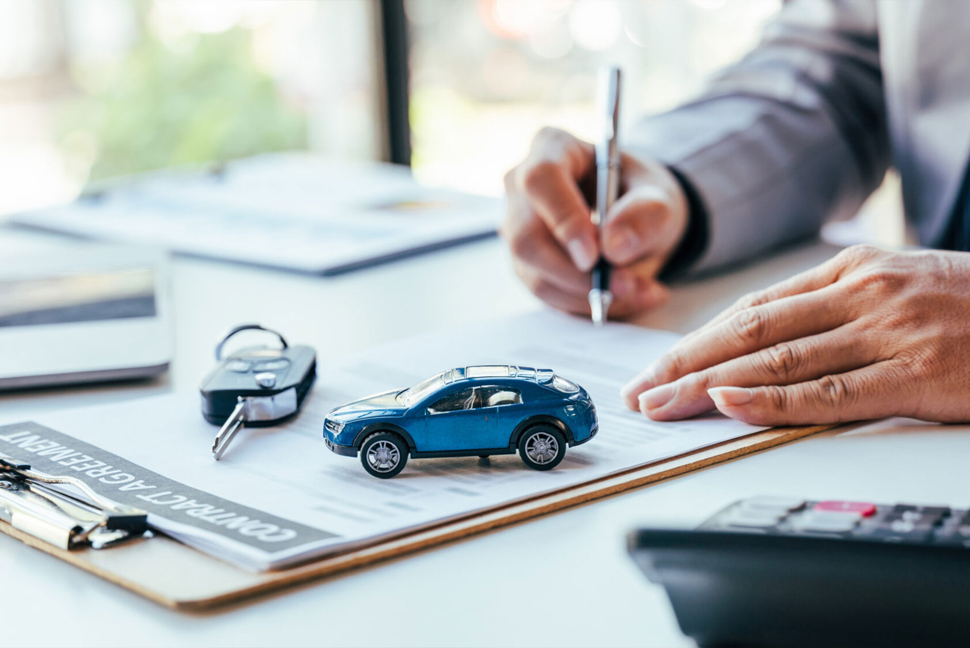 Toy car sitting next to keys on desk while person signs document.