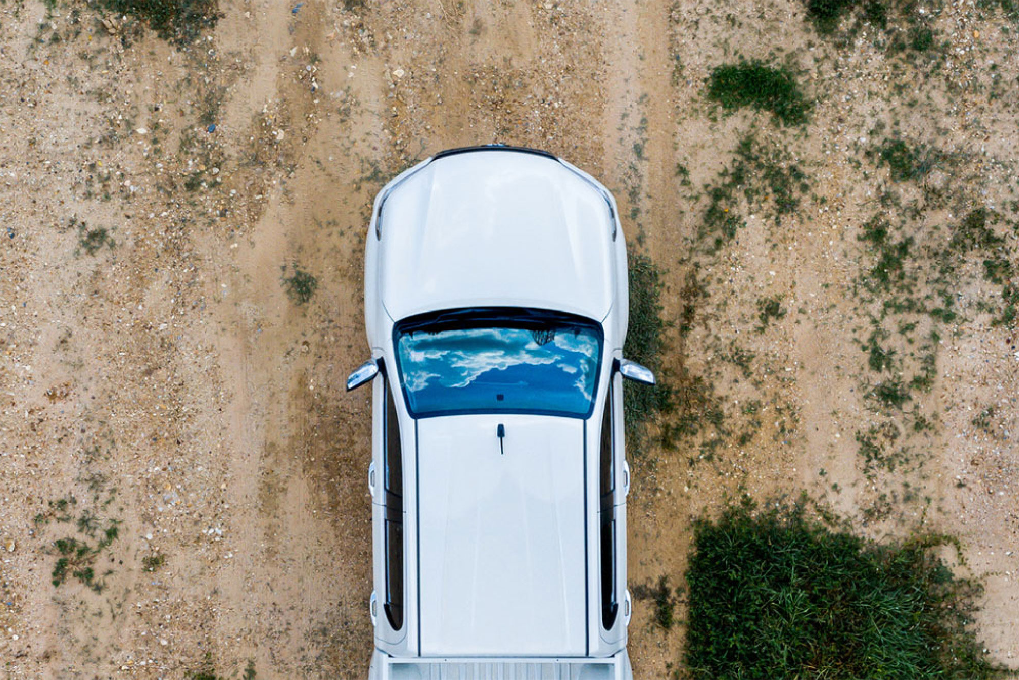 Aerial view of white car driving on dirt road.